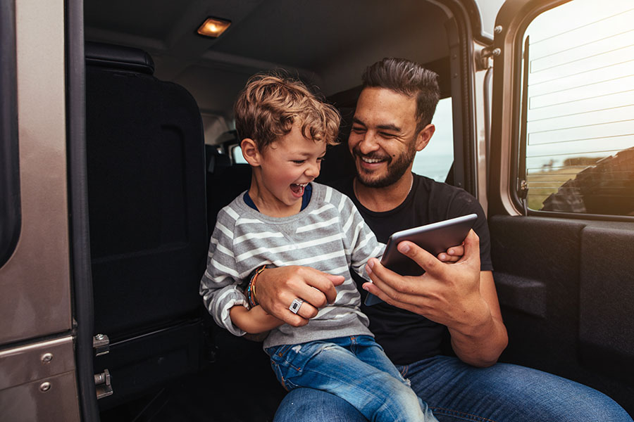 Client Center - Smiling Father and Son Sitting in Car on Roadtrip Using a Tablet