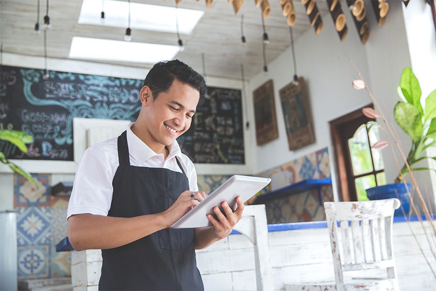 Business Insurance - Business Owner with Apron on Standing with Tablet in Modern Cafe